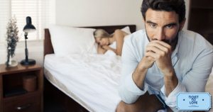 Tristezza post orgasmo: nell'immagine un uomo seduto sul letto con aria malinconica. La sua partner lo osserva in secondo piano, sotto le lenzuola