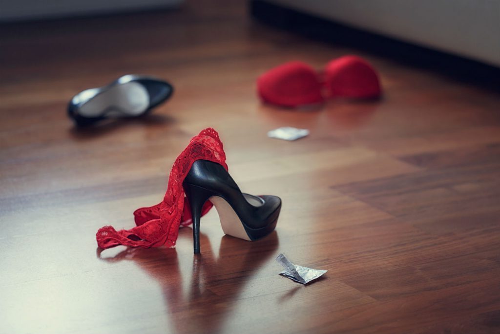 Storia del preservativo: nell'immagine la bustina di un condom aperta sul pavimento accanto ad una scarpa con tacco e lingerie femminile